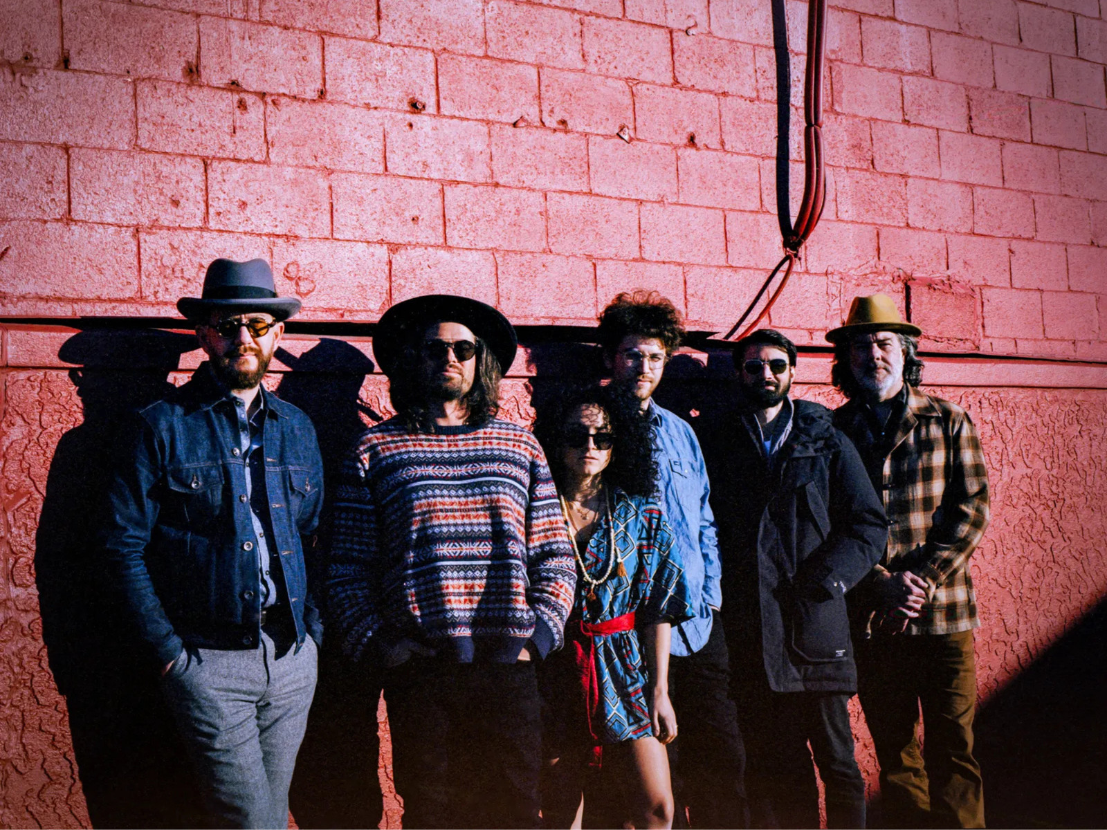 Members of Mojo Birds standing together in front of a red brick wall